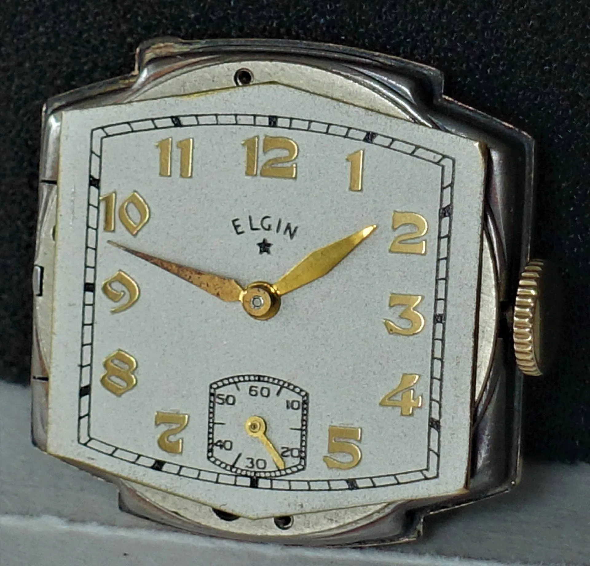Rechteckige Armbanduhr mit silberfarbenem Gehäuse, weißen Zifferblatt und goldfarbenen Zeigern sowie goldfarbenen Ziffern, kleine Sekunde bei sechs Uhr.