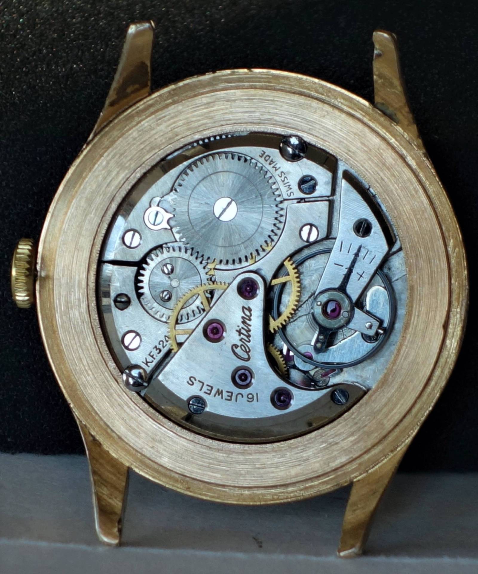 Silberfarbenes mechanisches Uhrwerk in einem goldfarbenen Uhrengehäuse.