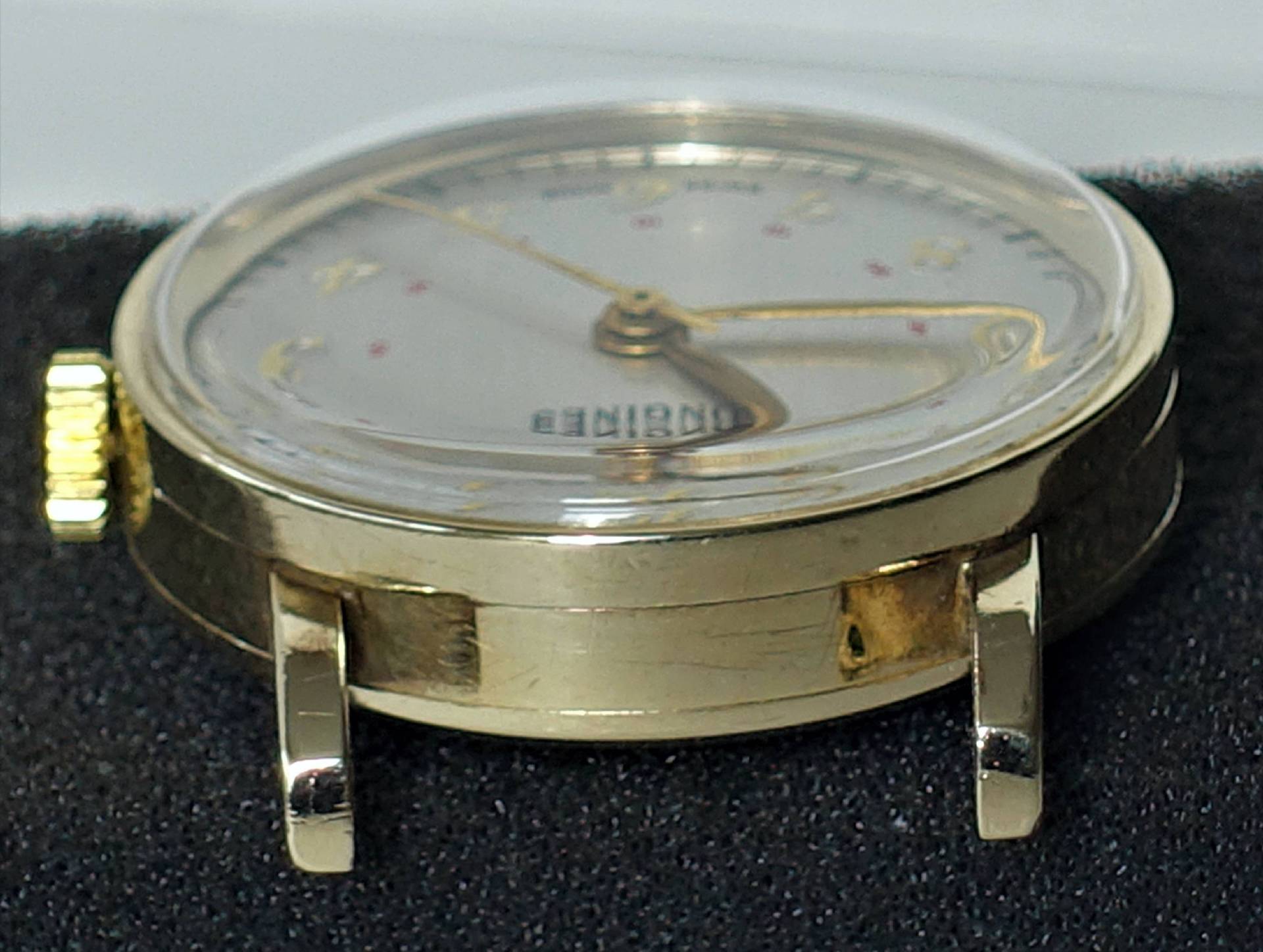 Detailansicht einer goldenen Armbanduhr mit hellem Ziffernblatt und goldenen Zeigern