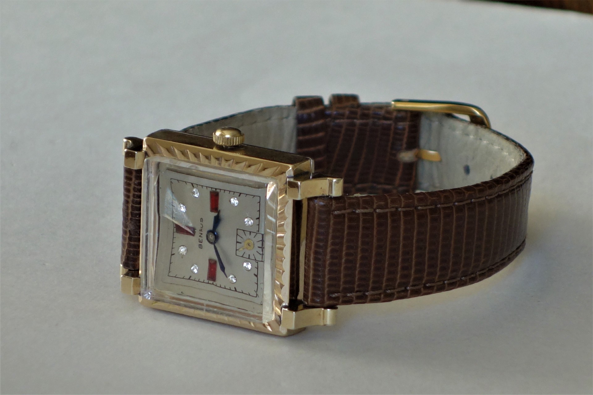 Rechteckige Armbanduhr mit goldfarbenem Gehäuse und braunem Lederarmband.