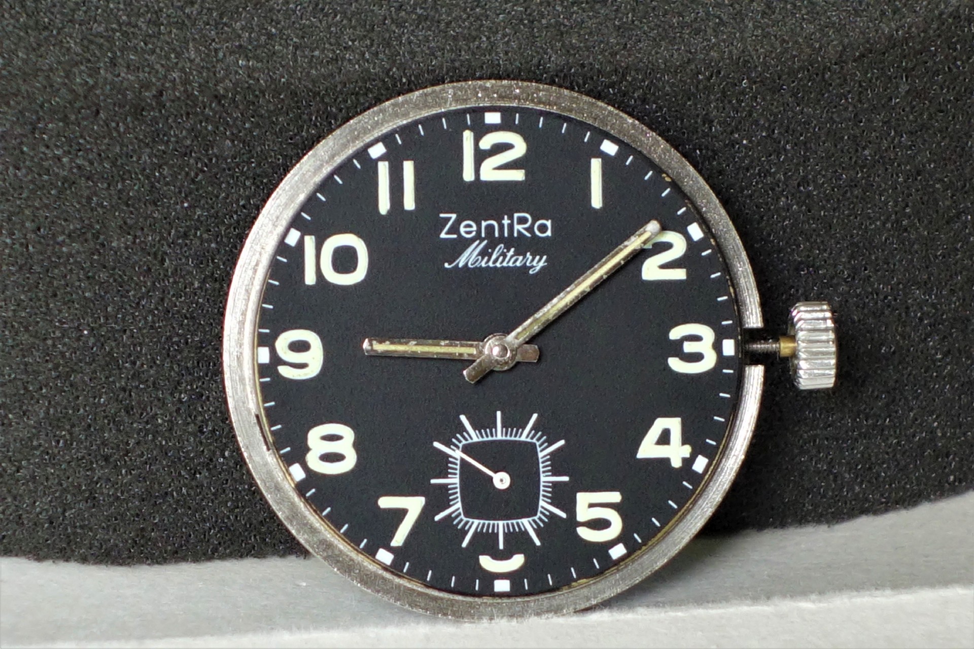 Schwarzes Uhrwerk mit weißer Beschriftung und silberner Krone, Zifferblatt mit arabischen Zahlen und kleiner Sekunde.