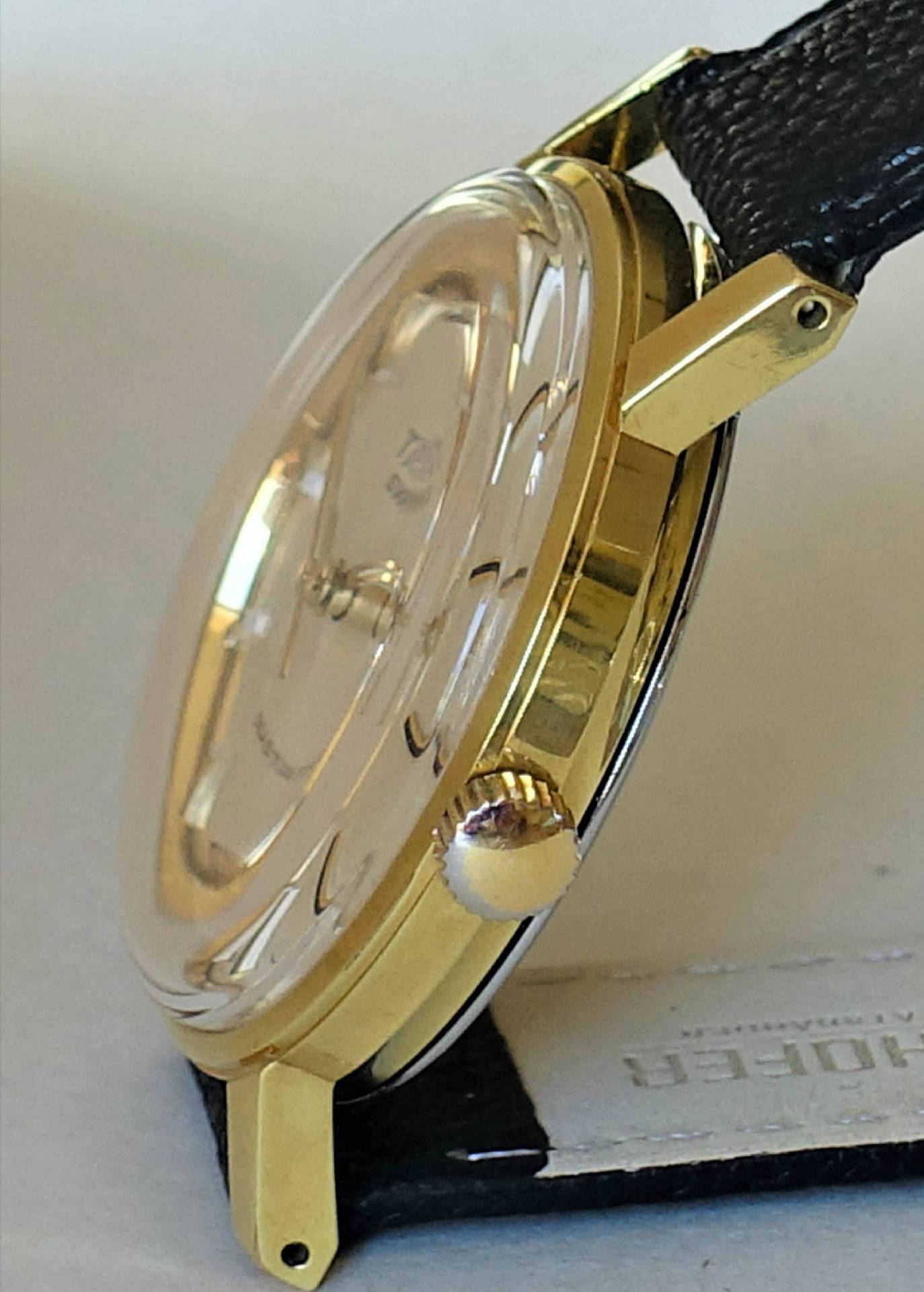 Flache Armbanduhr mit goldfarbenem Gehäuse und schwarzem Armband.